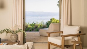 A room with a view of the sea, a wooden chair, a table with a vase, and a hanging light fixture. - Villa Delta Skiathos (Skiathos)