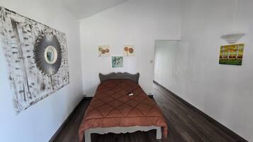 Quarto com cama, espelho e três quadros na parede.