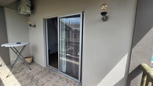 Un balcón con puerta corrediza de vidrio, una mesa pequeña y una planta en maceta.