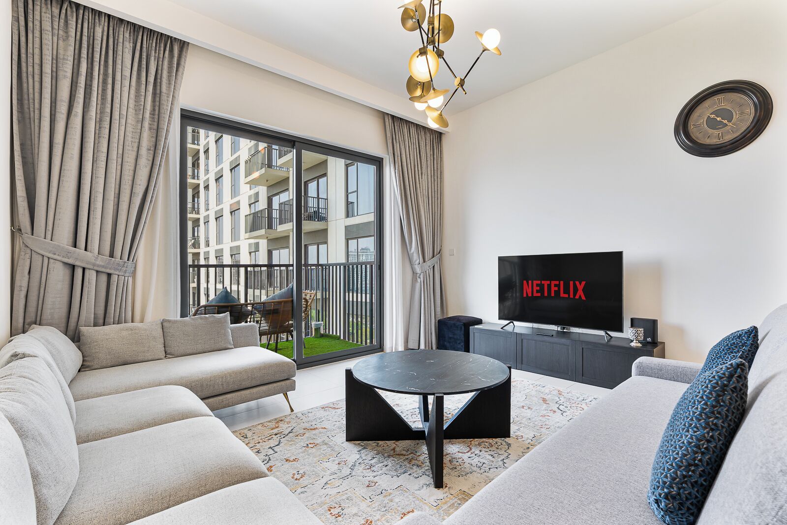 Uma sala de estar moderna com sofá, mesa de centro, televisão e varanda com cortinas.