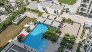 Vue aérienne d’un bâtiment moderne doté d’une piscine centrale, entouré d’espaces paysagers et de nombreux balcons.