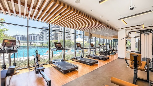 Une salle de sport moderne équipée de tapis de course, d’appareils d’exercice et de grandes fenêtres donnant sur un plan d’eau.