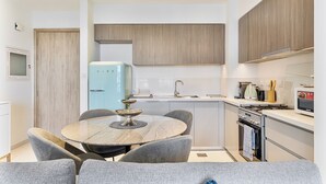 Une cuisine compacte avec une table de salle à manger ronde, des chaises à revêtement gris, un réfrigérateur bleu clair et des meubles de cuisine modernes.