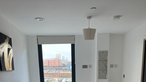 Ein modernes Schlafzimmer mit einem großen Bett und Blick auf die Stadt durch ein Fenster, wobei sich ein Stadtbild draußen zeigt.