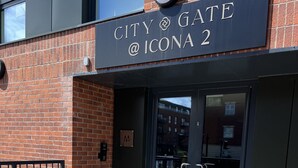Ein Gebäudeeingang mit einem Schild, auf dem 'CITY GATE @ ICONA 2' steht.