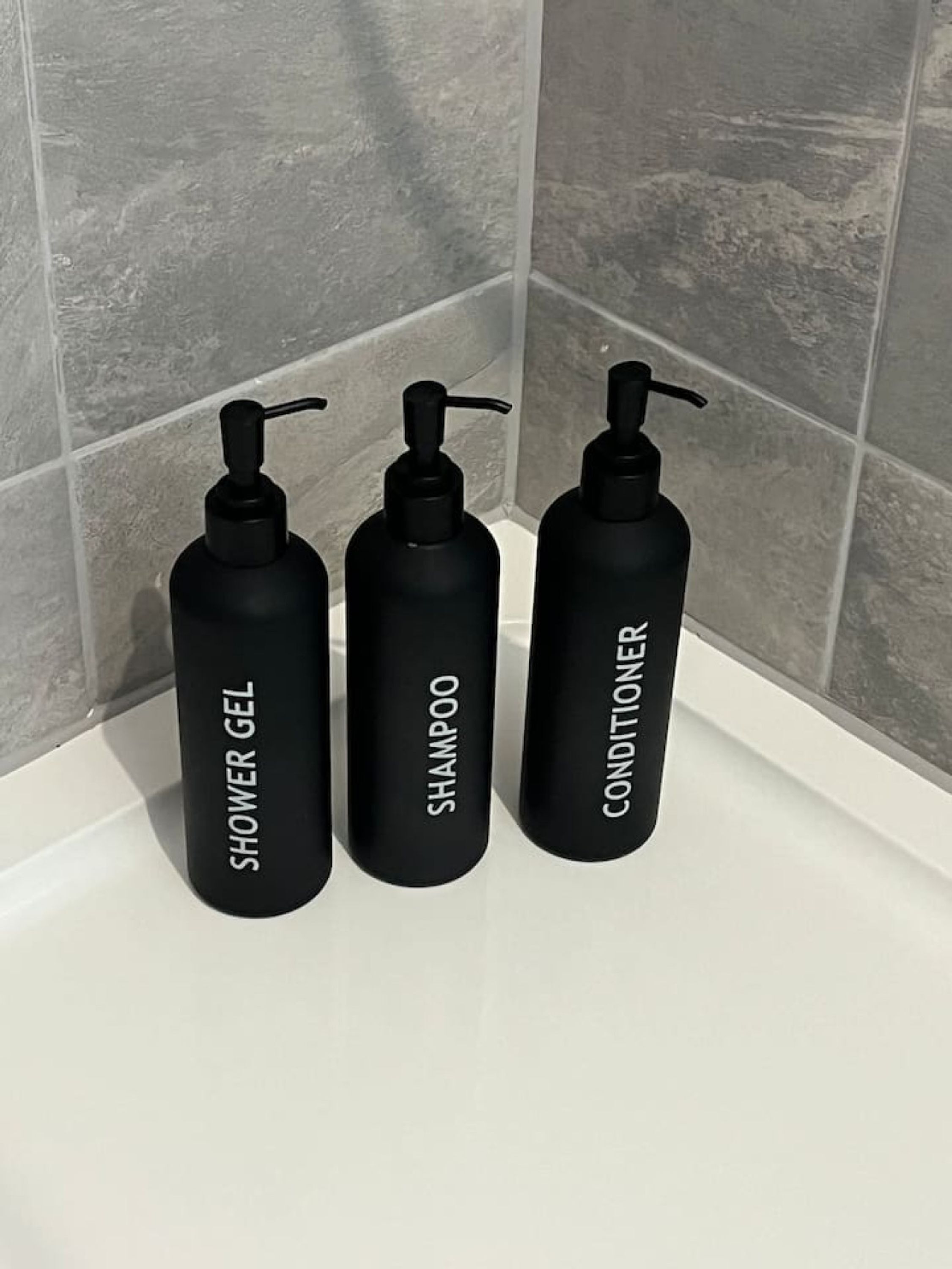 Three black bottles of shower gel, shampoo, and conditioner on a white surface.