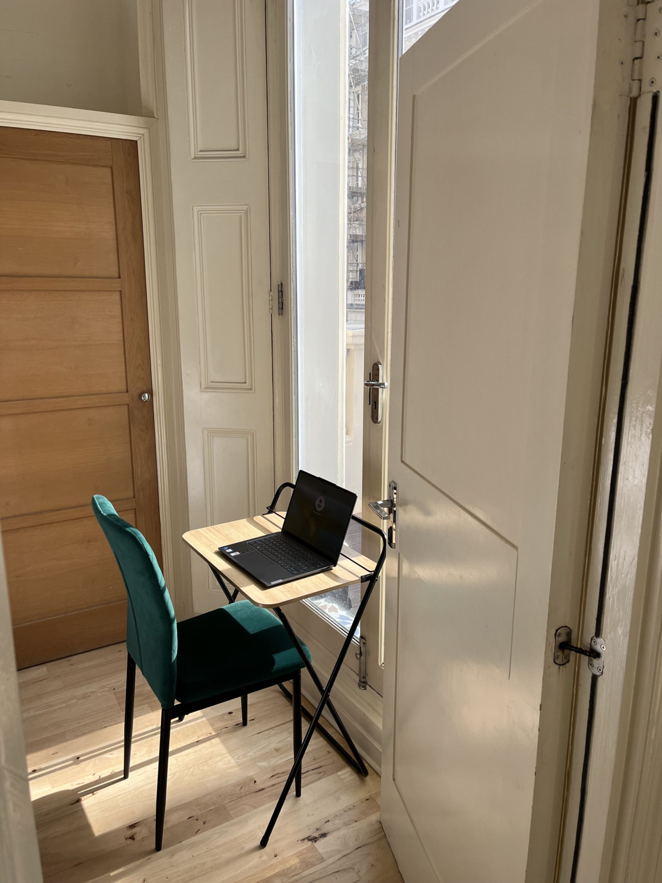A small workspace with a laptop on a foldable table, a teal chair, and a wooden door.