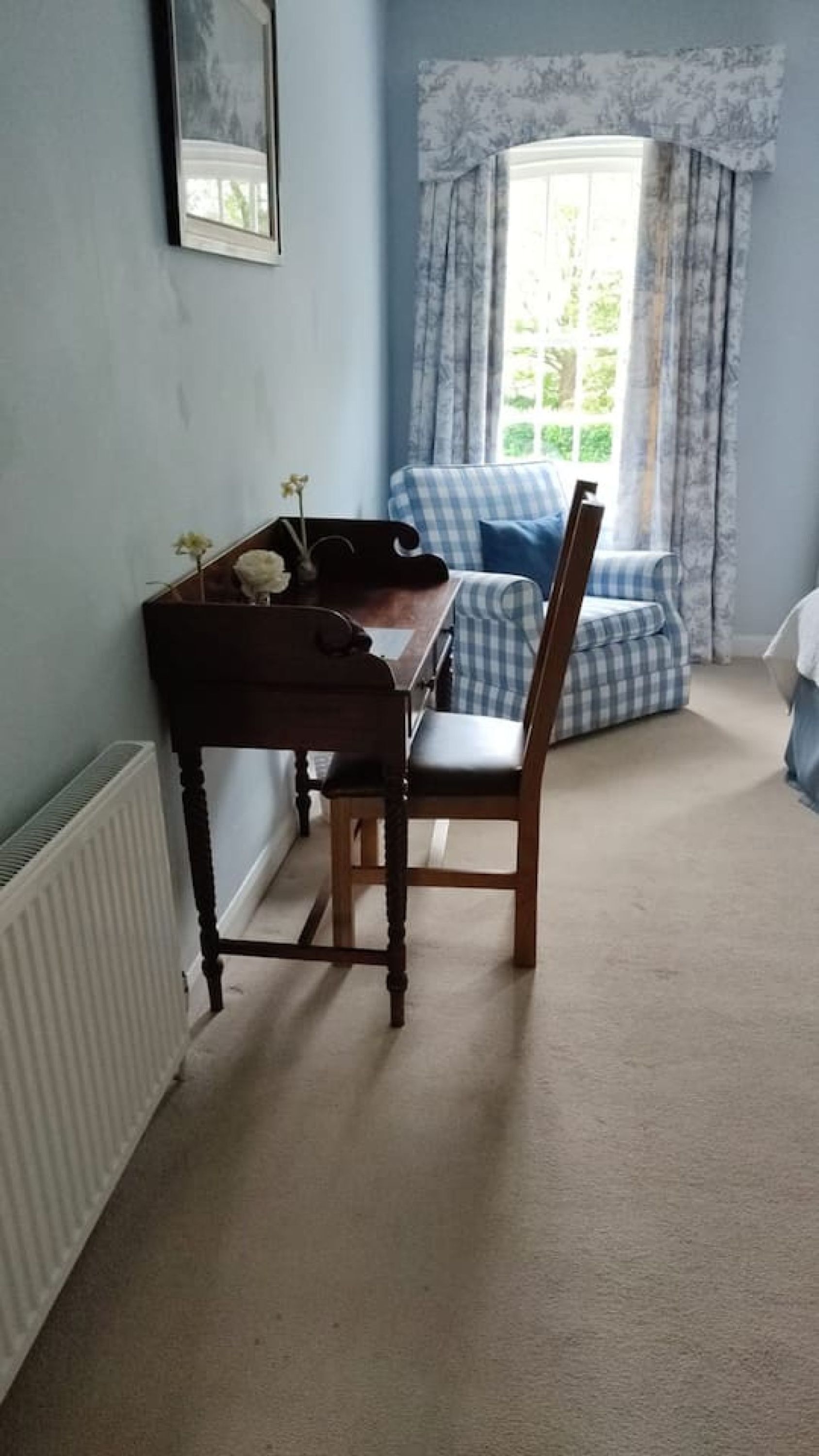 A room with a wooden desk, a chair, a radiator, a window with curtains, and a blue sofa.