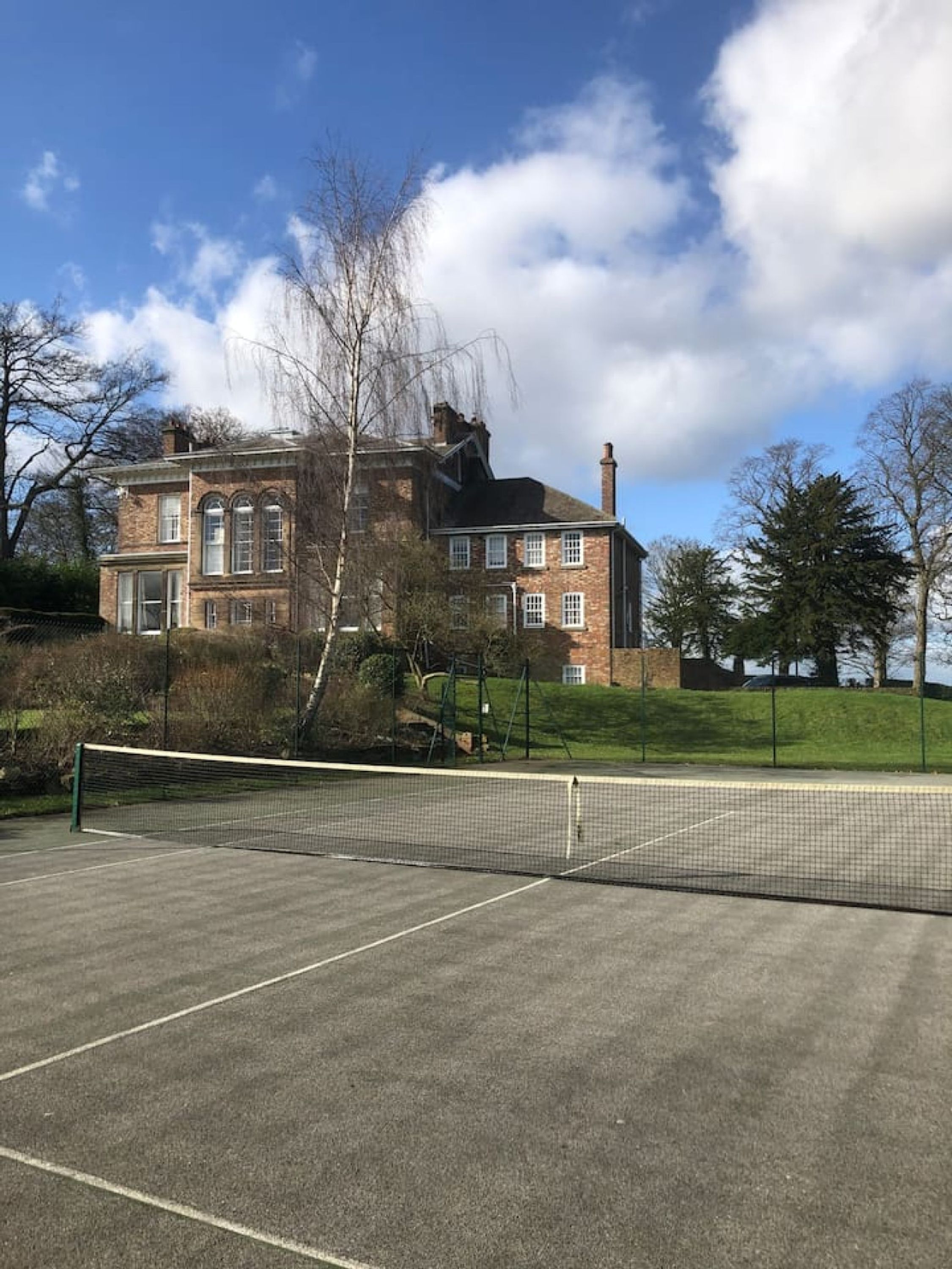 A tennis court with a net in front of a brick building with arched windows.