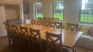 A dining area with a wooden table and chairs, a kitchen with a stove and cabinets, and large windows with a view of a green lawn. - Historic Hall Wing nr York Leeds Free Hot tub (Tadcaster)