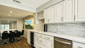 A modern kitchen with white cabinetry, a built-in oven, and a dining area with black chairs. - Grand Piano, Huge Geodes, Powerful Artistic Home (Dallas)