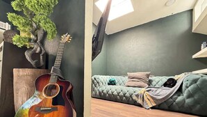 A room with a guitar, a cushioned sofa, and a wall-mounted TV. - Grand Piano, Huge Geodes, Powerful Artistic Home (Dallas)