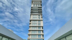 Un bâtiment moderne à plusieurs étages, doté d’une entrée centrale et entouré de murs de verre et de plantes en pot.