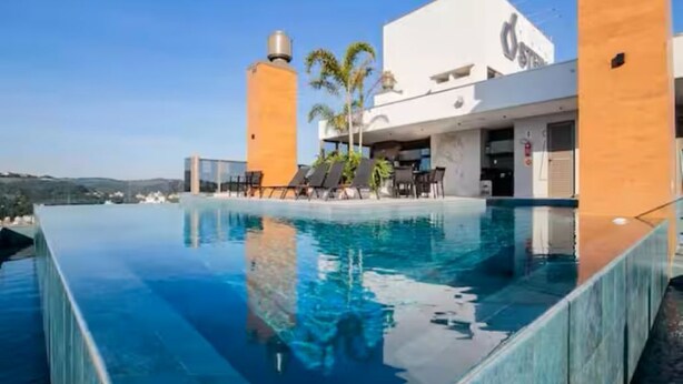 Un hôtel moderne doté d’une piscine à débordement sur le toit, de palmiers et offrant une vue dégagée sur les environs.
