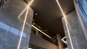 Un intérieur moderne agrémenté d’une installation lumineuse aux motifs géométriques, d’un comptoir d’accueil et d’un escalier.