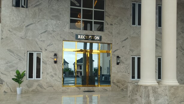 A marble reception area with a glass door, columns, and a potted plant.