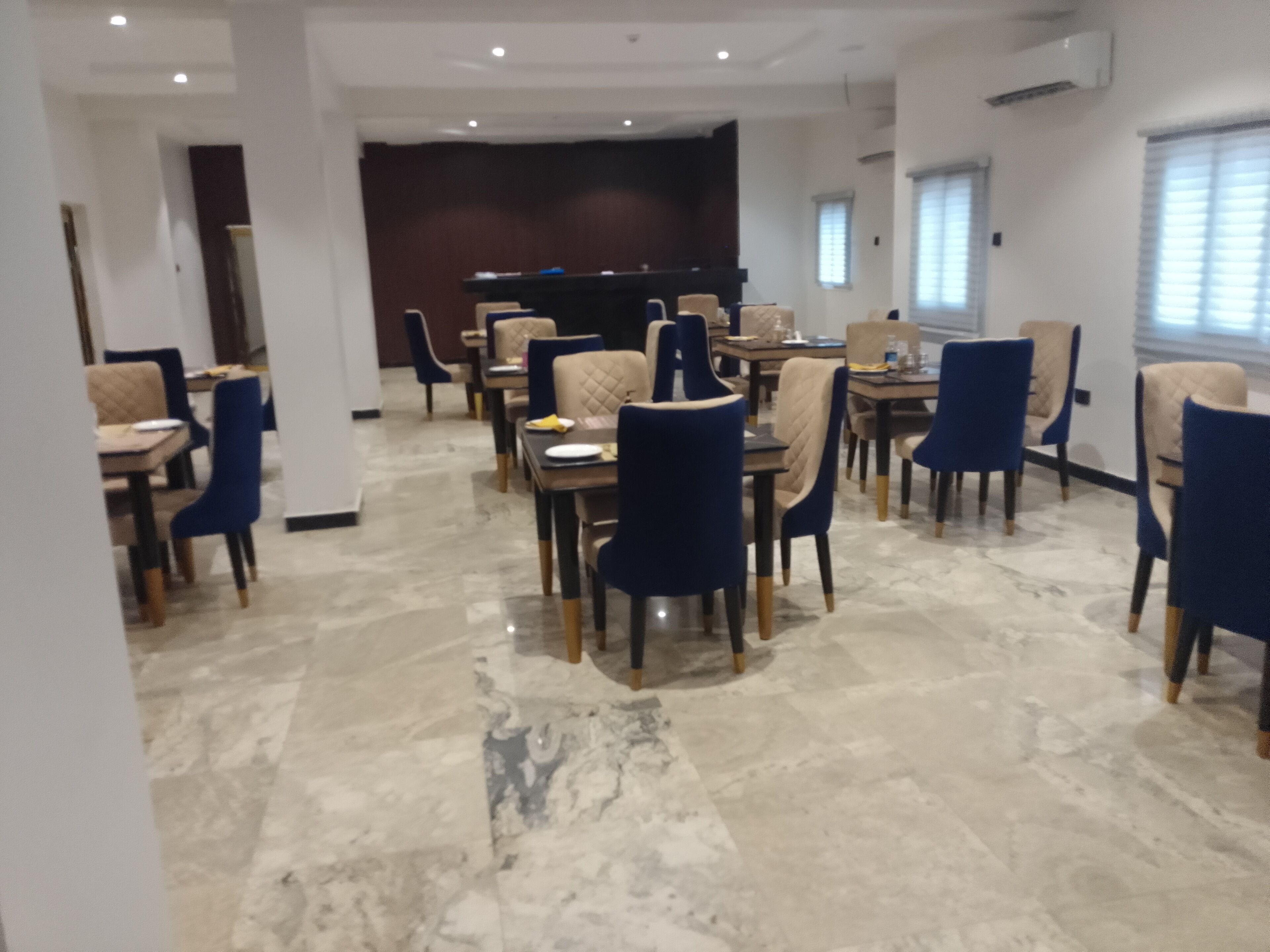 A spacious dining area with marble flooring, blue and beige chairs, and a dark wooden panel wall.