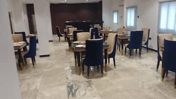 A spacious dining area with marble flooring, blue and beige chairs, and a dark wooden panel wall.