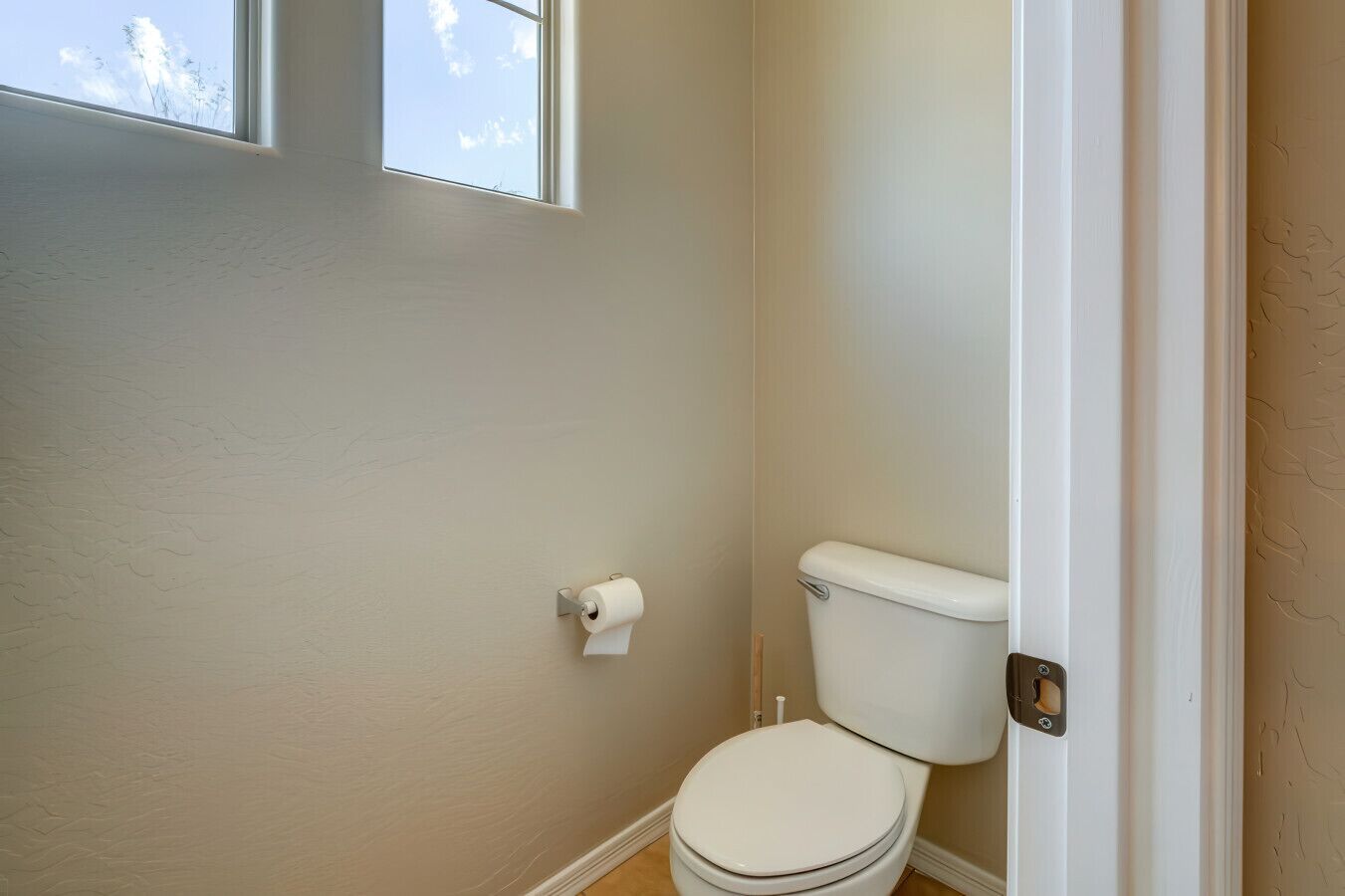 A small, clean bathroom with a toilet, a roll of toilet paper, and a window.