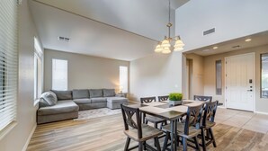 Un salon moderne avec un canapé d’angle gris, une table à manger avec des chaises et un lustre.