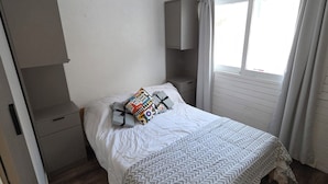 Un dormitorio con cama, mesita de noche, armario y ventana con cortinas.