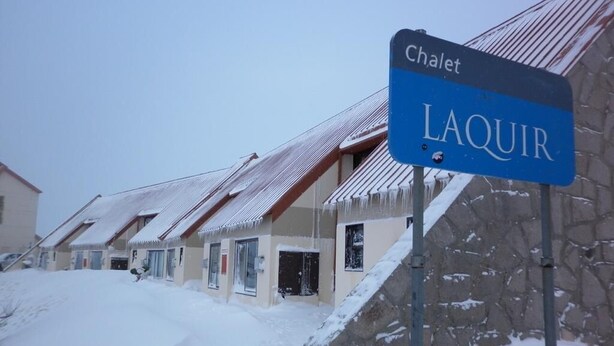 Señal de Chalet Laquir en un paisaje nevado con edificios cubiertos de nieve.