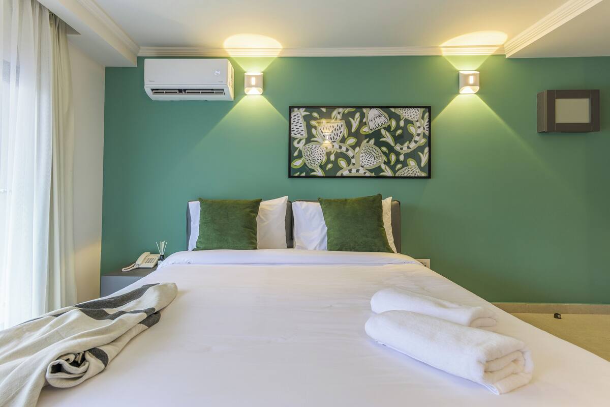 Habitación de hotel con cama, almohadas, una manta, toallas, aire acondicionado, teléfono de pared y una obra de arte en la pared.
