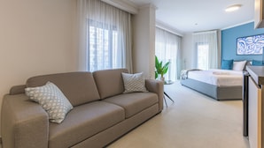 A modern hotel room with a sofa, a bed, a desk, and a large window with curtains. - CityZen - Boutique Studios in Achrafieh (Beirut)