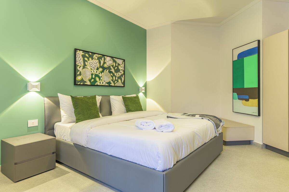 Un dormitorio moderno con cama, mesitas de noche y obras de arte en las paredes.