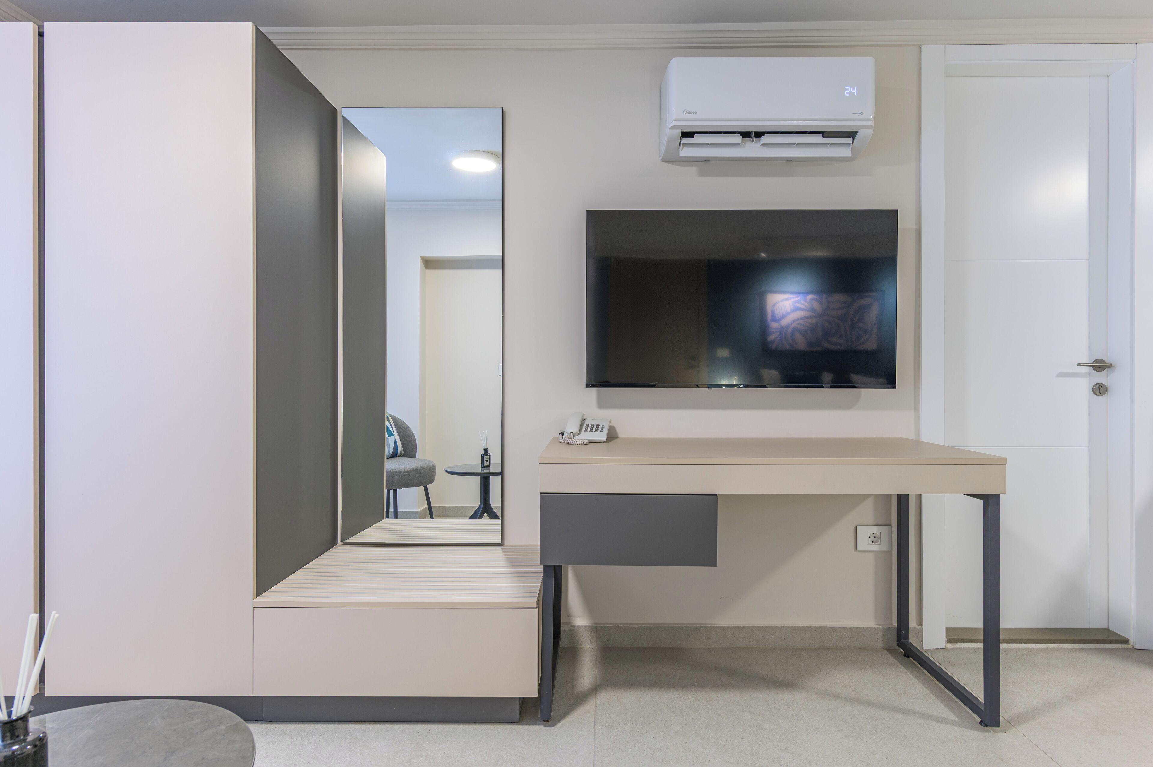 Une chambre moderne équipée d’un bureau, d’un téléviseur à écran plat fixé au-dessus, d’un miroir et d’une porte.