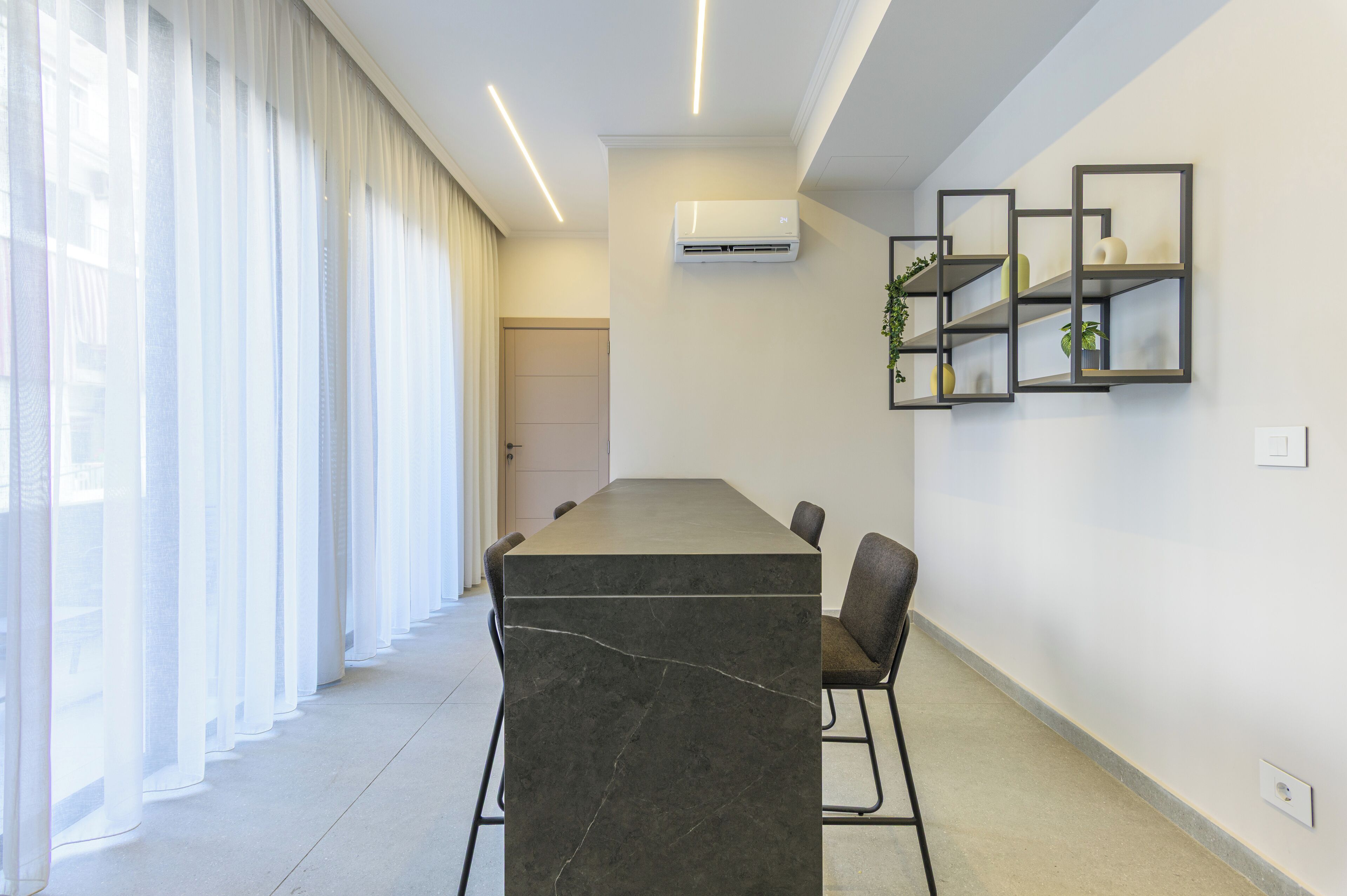 Una sala de conferències moderna amb una taula de marbre, cadires negres, un aire condicionat blanc i una finestra amb cortines translúcides.