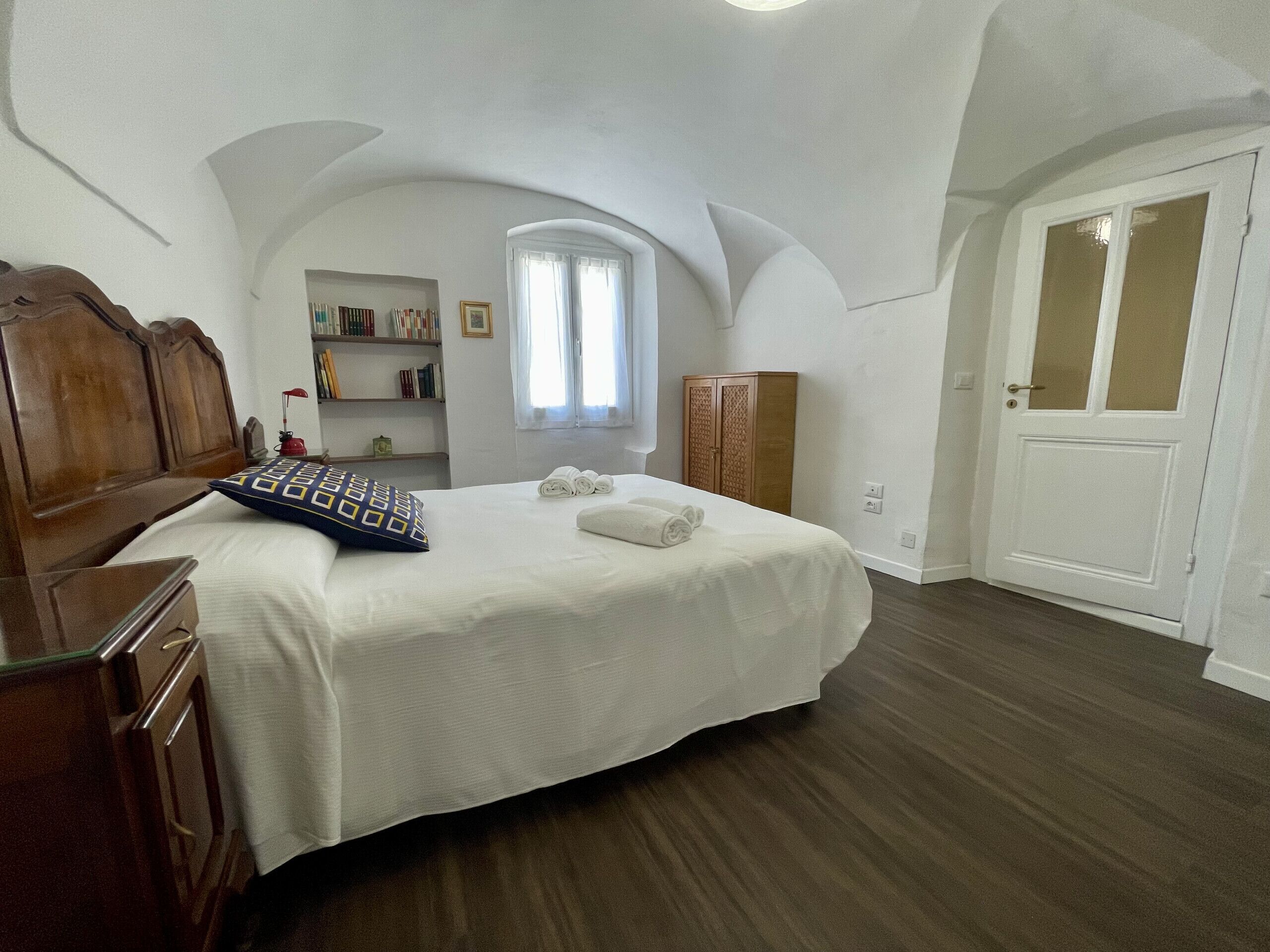 Un dormitorio con cama de madera, un armario, una ventana pequeña y una puerta.
