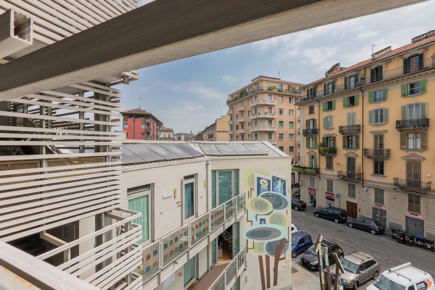A multi-story building with balconies, a street view, and parked cars.