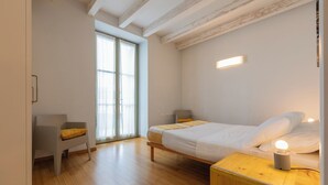 Un dormitorio con cama, mesitas de noche, una silla, un ventanal con cortinas y techo de madera.