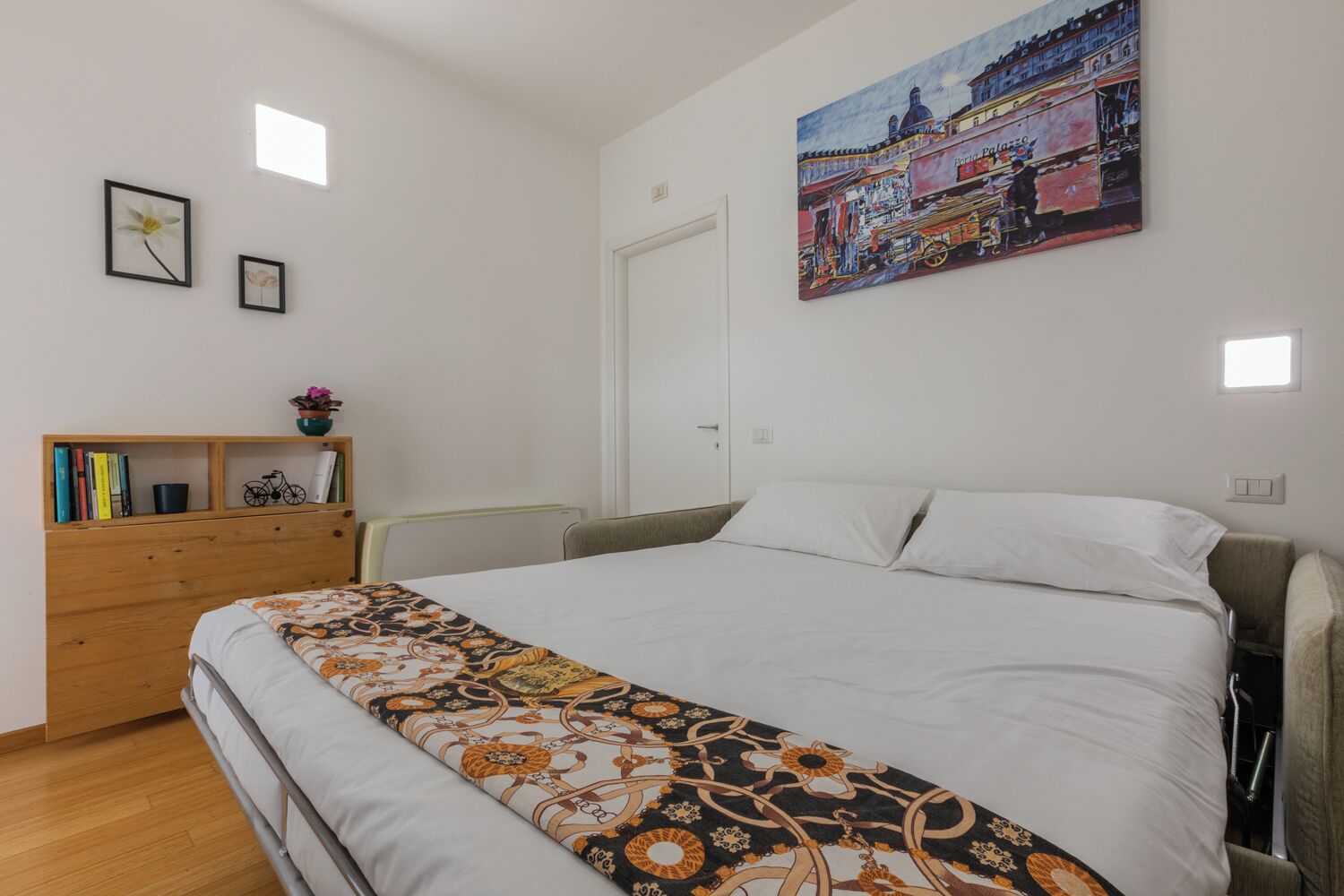 Un dormitorio con cama, cómoda de madera, estantería y un cuadro en la pared.
