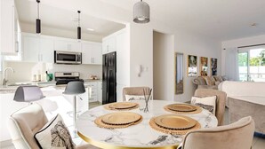 Una cocina moderna con armarios blancos, microondas y refrigerador. Hay un comedor con una mesa redonda y sillas.