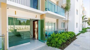 Un hotel moderno con fachada de vidrio, balcón y un jardín bien cuidado.