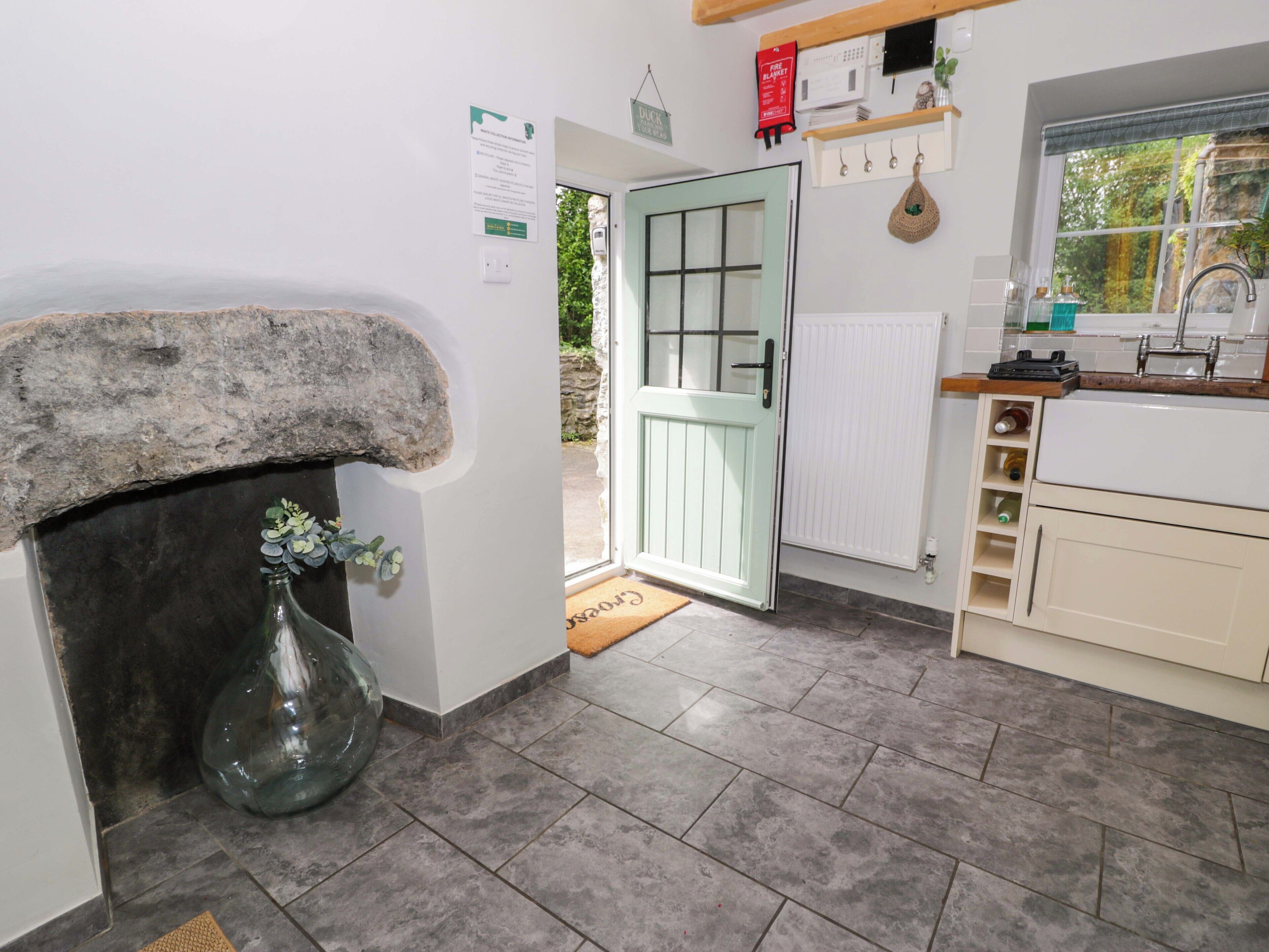 Cozinha com lareira de pedra, porta para o exterior e janela com vista para o verde.