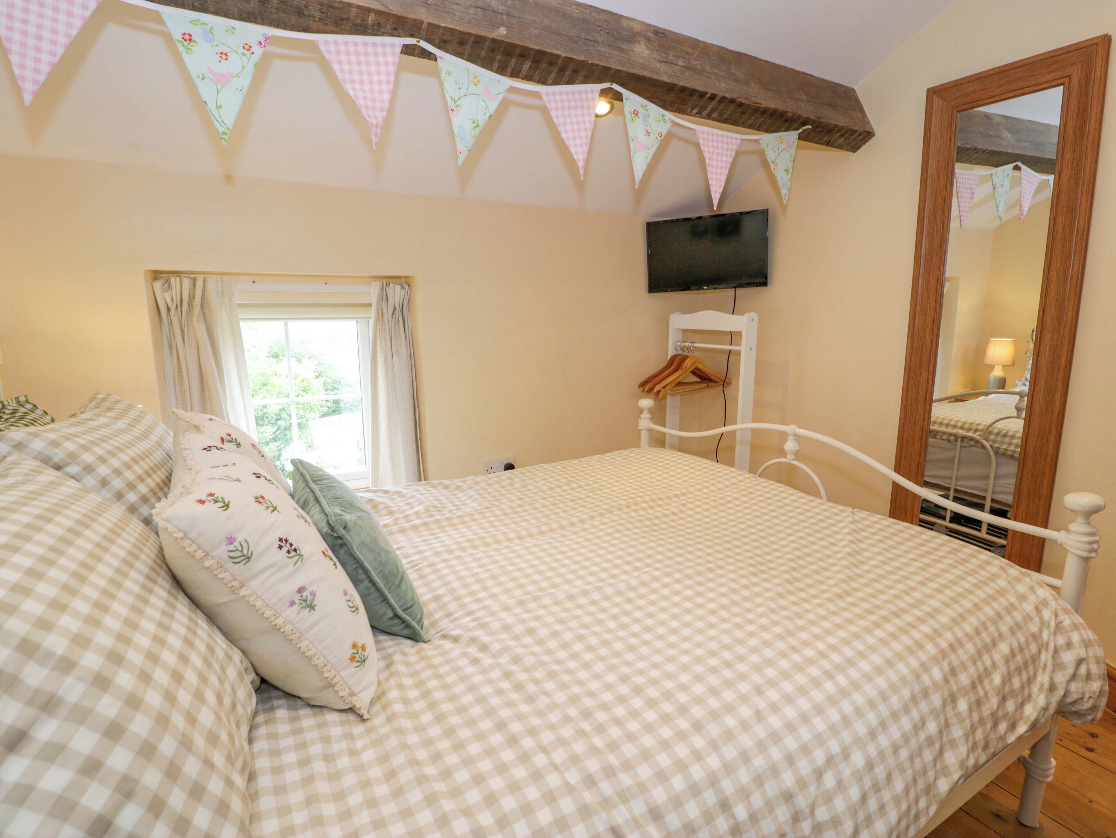 A bedroom with a checkered bedspread, a wooden headboard, a television mounted on the wall, and a window with curtains.