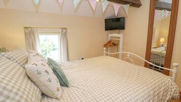 A bedroom with a checkered bedspread, a wooden headboard, a television mounted on the wall, and a window with curtains.