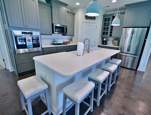 A kitchen with a central island, bar stools, a microwave, a refrigerator, and a pendant light.
