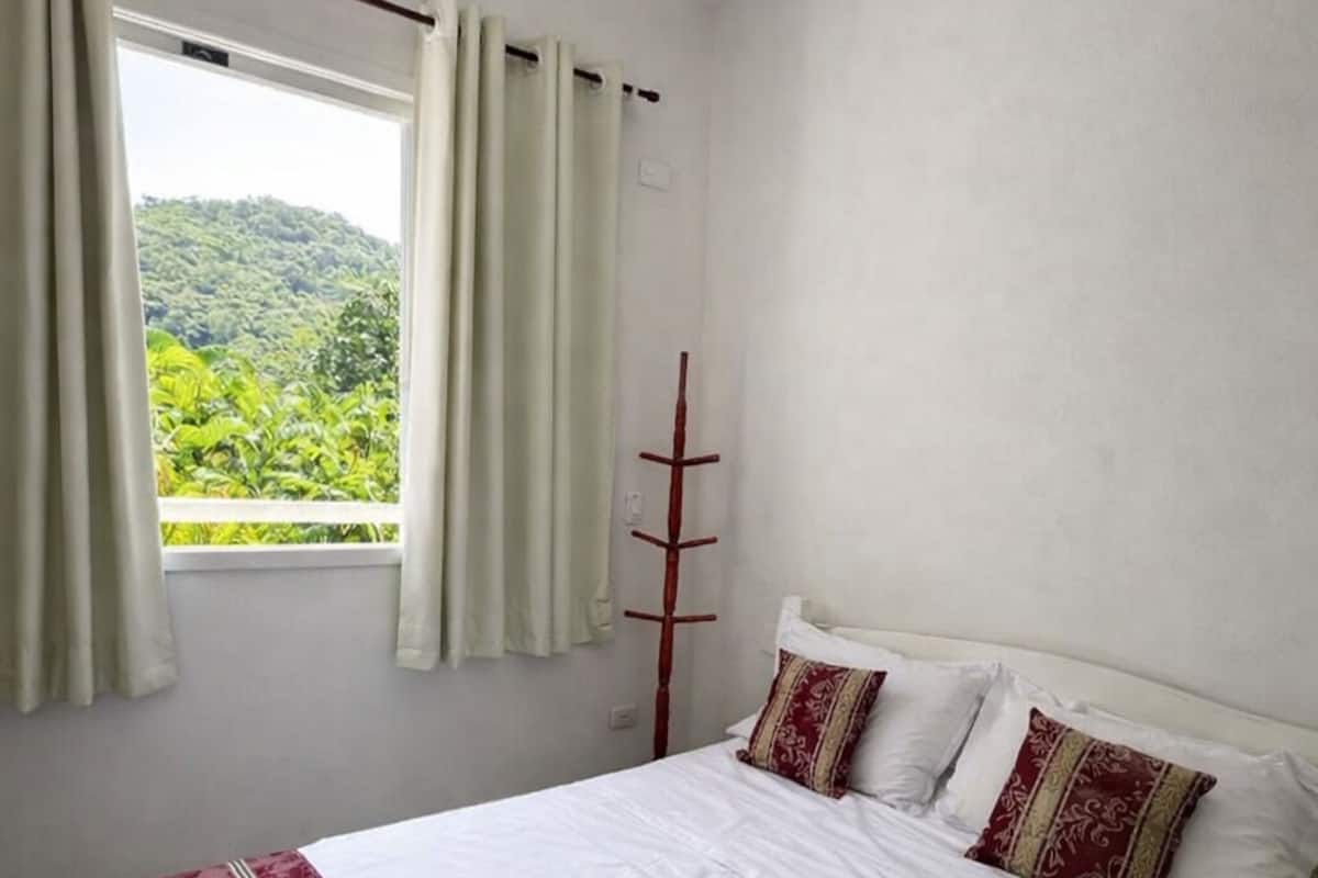 Un dormitorio con una cama grande, paredes blancas y una ventana con cortinas.