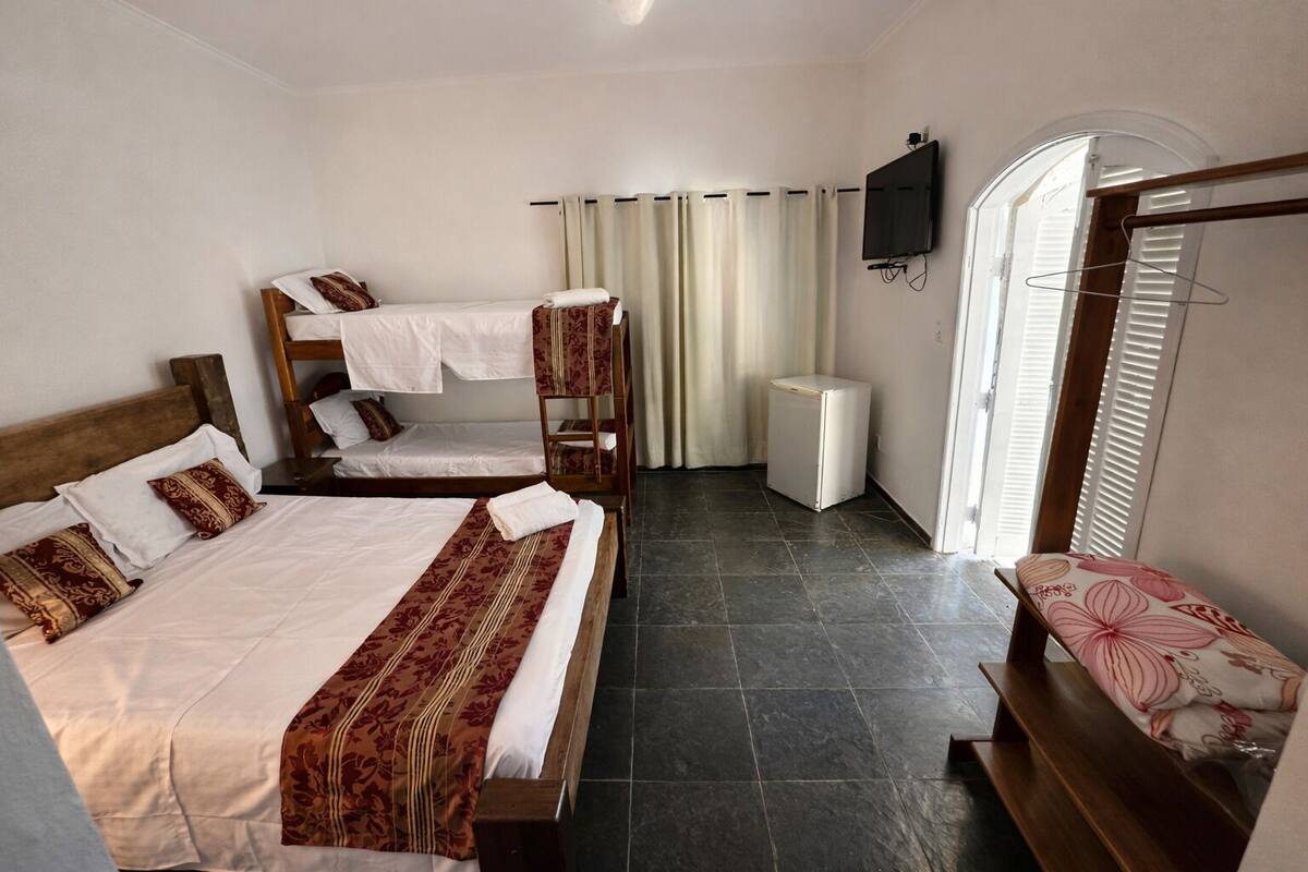 Habitación de hotel con dos camas, televisión, refrigerador pequeño y un banco con cojín floral.