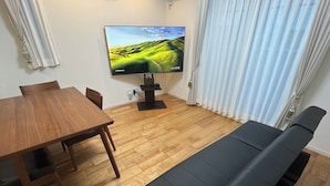A living room with a wooden dining table, a black sofa, and a flat-screen TV on a stand. - One private house! Max. 9 people with parking! 3 min walk from Yoyogi, 2 min by train from Shinjuku/Harajuku, 5 min from Shibuya, 7 min from Roppongi Hotel Like Yoyogi Homes (Sibuya-ku)