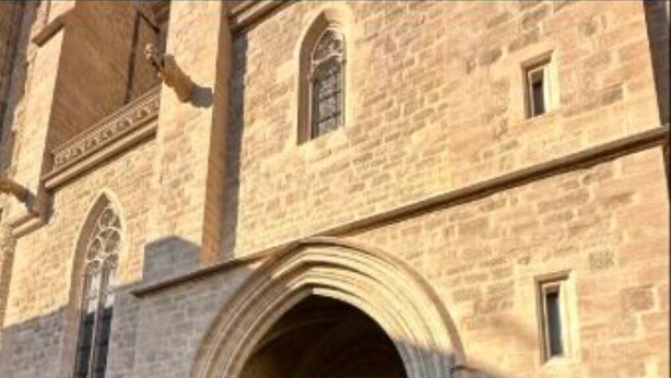 Un edificio de piedra con una entrada arqueada, una ventana pequeña y una cartelera.