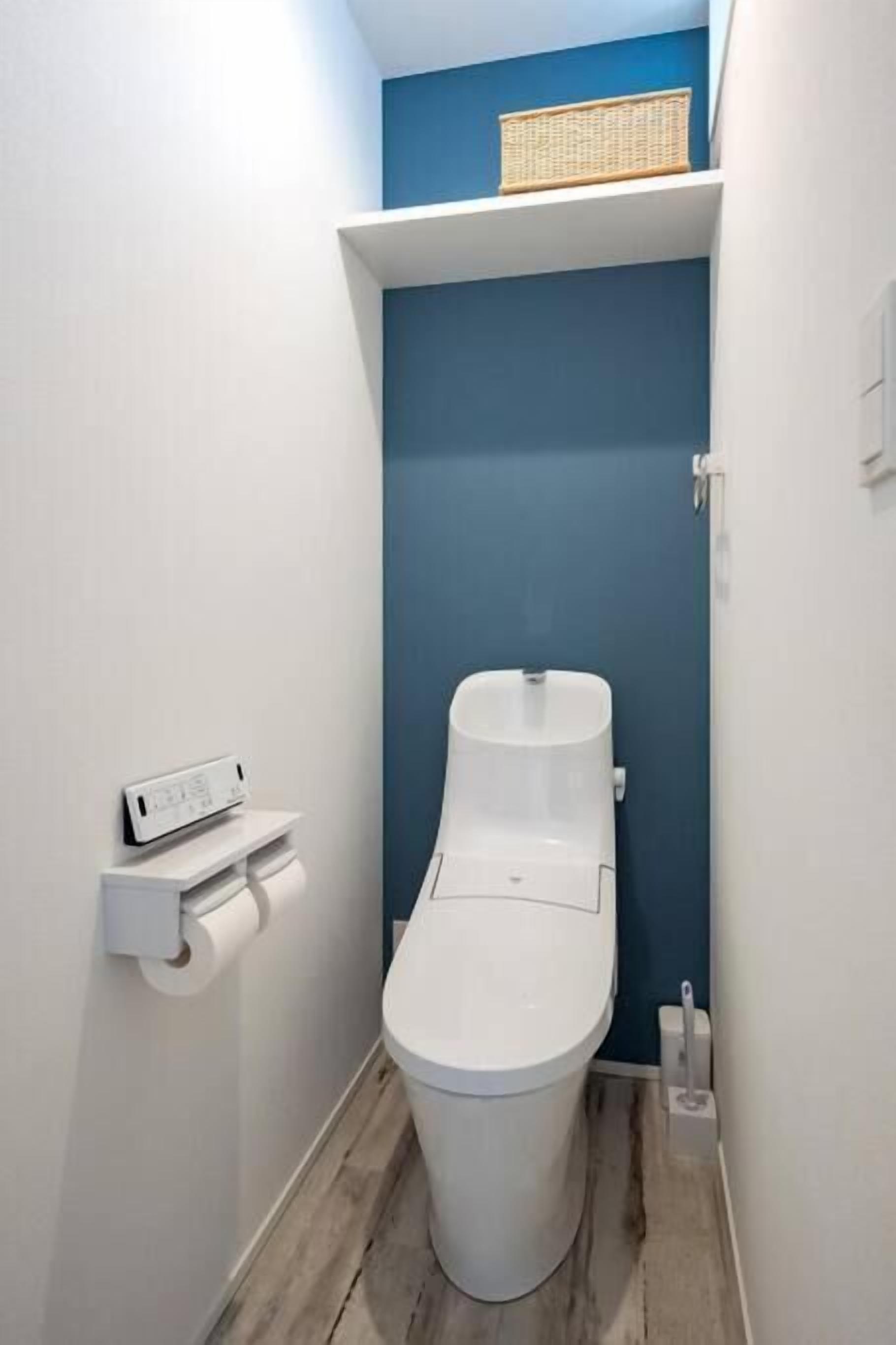 A compact bathroom with a white toilet, a blue accent wall, and a small shelf with a basket.