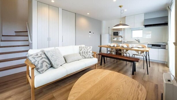 A modern apartment with a white sofa, wooden dining table, and a kitchen area with white cabinets and a microwave.
