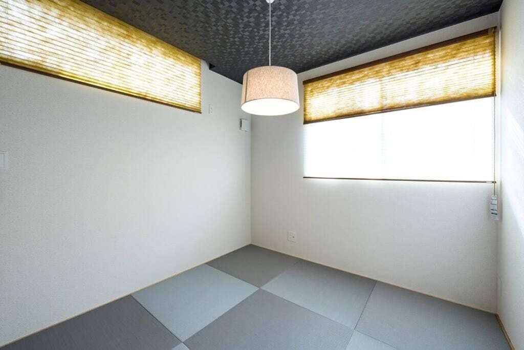 Una habitación con suelo de tatami, una lámpara de techo y una ventana con persiana.