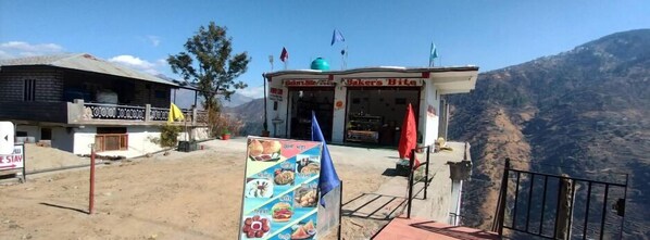 A small roadside eatery named "Baker's Bite" with a signboard displaying various food items. - Hatu View Homestay (Kumharsain)