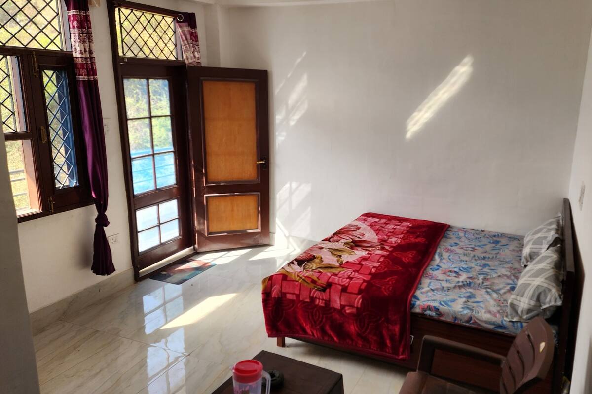 A small, well-lit room with a bed, a window with curtains, and a door.